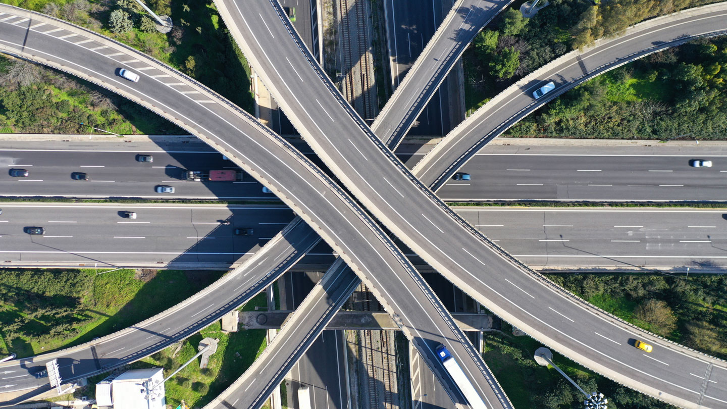 Aerial view of a highway interchange with multiple overpasses and several vehicles on the roads surrounded by green vegetation.